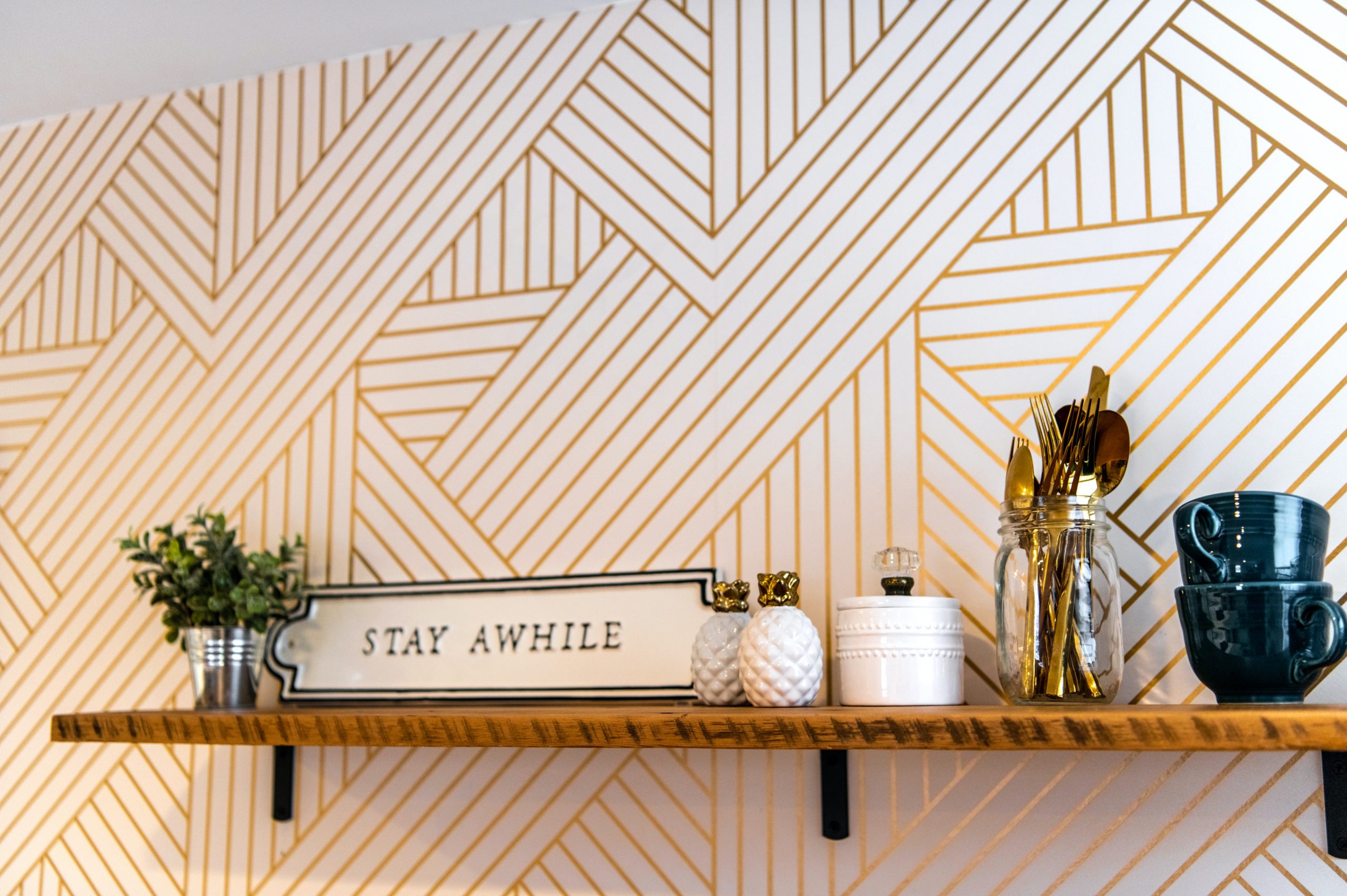 Gold patterned wallpaper with a wooden shelf and cups